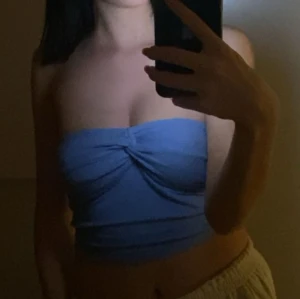 Blå tubtopp - Säljer en snygg blå tubtopp som är perfekt för sommaren. Den har en enkel men stilren design med en liten twist framtill som ger en fin detalj. Toppen är axelbandslös och passar perfekt till både fest och vardag.