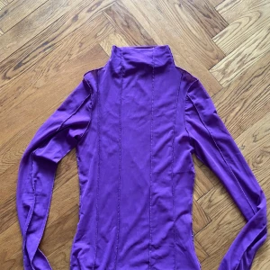 Lila långärmad topp i mesh - Snygg lila topp i mesh med långa ärmar. Tröjan har en hög krage och är figurnära, vilket gör den både bekväm och trendig.