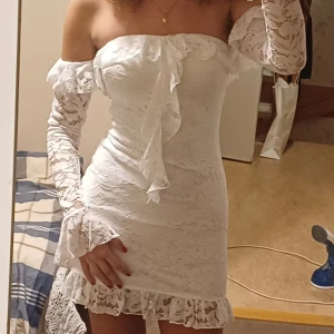 Vit spetsklänning - Säljer en helt oanvänd vit spetsklänning med offshoulder-design (ärmarna är separerade från klänningen). Klänningen har volangdetaljer. Perfekt för speciella tillfällen!