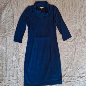 Mörkblå klänning med polokrage - Snygg mörkblå klänning från Wow to Go med en elegant polokrage. Klänningen har långa ärmar och en stilren design som passar perfekt för kyligare dagar. Den är tillverkad i ett mjukt material med ett diskret mönster som ger en extra touch.