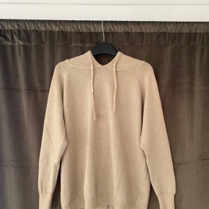 Beige hoodie med huva - Säljer en stilren beige hoodie med huva och dragsko. Tröjan har långa ärmar och ribbade muddar vid ärmslut och nederkant. Perfekt för en avslappnad look. Merinoull tyg!!! Priset är inte hugget i sten!!