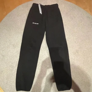 Svarta mjukis/träningsbyxor från CCM - Svarta mjukis/träningsbyxor från CCM med elastisk midja och snörning. Perfekta för en avslappnad stil. Byxorna har en enkel design med CCM-logga på benet. Mycket bra skick! Passar till allt, bara höra av sig vid frågor!