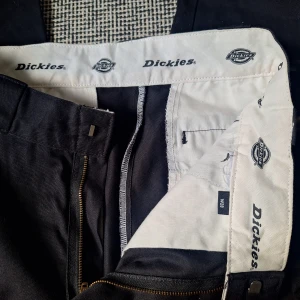 Svarta byxor från Dickies - Snygga svarta byxor från Dickies i klassisk stil. Byxorna har en rak passform och är tillverkade i slitstarkt material. Perfekta för en stilren look med praktiska fickor och dragkedja. Aldrig använt!