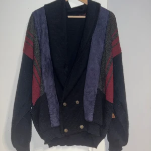 Svart kofta från King - Säljer en unik svart kofta från King med färgblock i rött, grått och blått. Koftan har en dubbelknäppning med metallknappar.