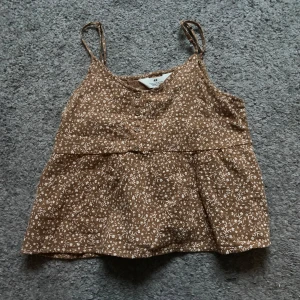 Brun blommig linnetopp från H&M - Säljer en söt brun linnetopp från H&M med vita blommor. Perfekt nu till våren! 