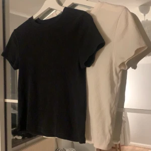 Svart och vit ribbad t-shirt - Två stilrena t-shirts i svart och vitt med ribbad struktur. Perfekta för en enkel och snygg look. Kortärmade och i mjukt material för bekväm passform.
