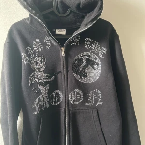 Svart hoodie med tryck från Aim for the Moon - Snygg svart hoodie med dragkedja från aim’n for the moon. Sällsynt hoodie med rhinestones i storlek s säljer pågrund av att den är liten för mig. PRISET är inte hugget i sten och går att diskutera vid snabb affär😀