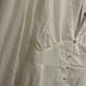Student/ Vit klänning - Elegant vit klänning från med v-ringning och långa ärmar. Klänningen har en rad knappar framtill och en smickrande passform. Perfekt för studenten eller en sommardag. Helt ny men passade tyvärr inte på mig. 