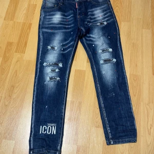 Blåa dsquared - Snygga blå jeans med slitningar och coolt tryck på ena benet. Jeansen har en avslappnad stil med en unik design av färgstänk och broderad detalj på bakfickan. Perfekta för en trendig look.