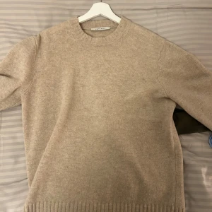 Beige stickad tröja från A Day's March - Säljer en stilren beige stickad tröja från A Day's March. Tröjan har en rund halsringning och ribbade muddar vid ärmslut och nederkant. Perfekt för kyligare dagar.