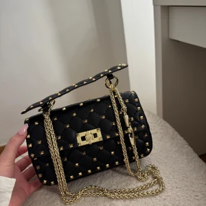 Valentino garavani väska med nitar - Säljer min valentino då den ej kommer till användning. Den är helt oanvänd då jag fått den i present får nåt år sedan, men en aning för liten för min smak. Den är självklart äkta och det medföljer ett äkthetsbevis samt dustbag. Säljer den billigt då den bara står hemma och ej används, fast pris 2500kr eller bud!