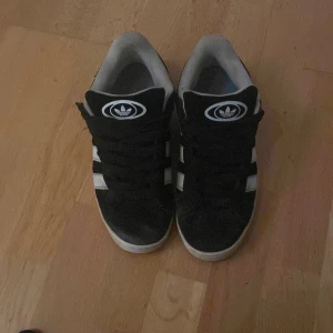Adidas campus 00 - Säljer ett par svarta campus 00 med svarta snören i ganska bra skick, vi snabb affär kan priset diskuteras, tveka inte på att höra av er
