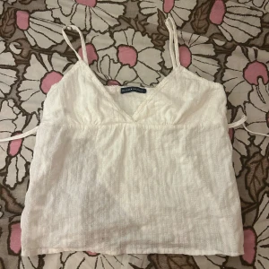 Vit linnetopp från Brandy Melville - Säljer en så söt vit linnetopp från brandy melville!Toppen har smala axelband och knytning där bak. Den är helt perfekt till sommar/vår💗💗Jag säljer då den inte kommer till användning. Det är bara att skriva ifall du undrar över något!!!