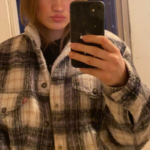  jacka  - Säljer en snygg rutig jacka från Levi's i storlek M. Jackan har en mysig teddyfoder och knappar framtill. Perfekt för kyligare dagar med sin stilrena design och bekväma passform.