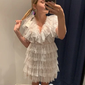 Vit spetsklänning med volanger - Säljer eventuellt beroende på vilken efterfrågan!Använd 2 gånger och köpt på united fashion. Super fin vit spetsklänning med volanger och v-ringad design. Klänningen har korta ärmar och en kort längd. 