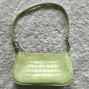 Ljusgrön axelväska med krokodilmönster - Snygg ljusgrön axelväska med krokodilmönster och dragkedja. Perfekt för att ge en färgklick till din outfit. Väskan har en justerbar axelrem och är tillverkad i syntetmaterial.