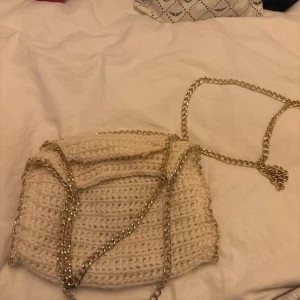 Virkad liten väska med kedja  - Säljer en snygg beige stickad axelväska med en stilren kedja som axelrem.Väskan är rymlig nog för dina nödvändigheter och har en mjuk, handgjord känsla.Ser smutsig ut på bild är ej det i verkligheten.