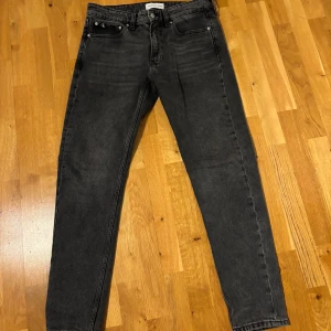 Grå jeans från Calvin Klein - Snygga grå jeans från Calvin Klein med klassisk femficksdesign och diskret CK-logga på baksidan. Perfekta för en stilren look. De har en rak passform och är tillverkade i ett slitstarkt material.