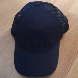 Svart keps från Calvin Klein - Snygg svart keps från Calvin Klein med broderad logga framtill. Kepsen har ett nätmaterial på baksidan för bättre ventilation och justerbar passform. Perfekt för en stilren look.