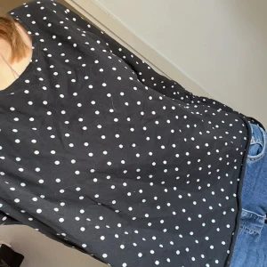 Svart prickig blus - Säljer en svart blus med vita prickar. Blusen har långa ärmar med elastiska muddar och en avslappnad passform. Perfekt för en stilren look.