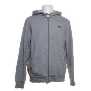 Grå hoodie från Puma - Säljer en grå hoodie från Puma med dragkedja och huva. Den har en liten svart logga på bröstet och praktiska fickor framtill. Perfekt för en avslappnad stil.