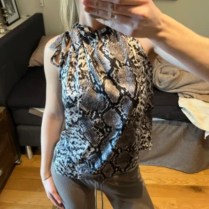 Ormmönstrad topp från SHK Paris - Snygg ormmönstrad topp från SHK Paris i svart och vit. Toppen har en halterneck-design med knytband vid axlarna och är ärmlös. Perfekt för en trendig look!