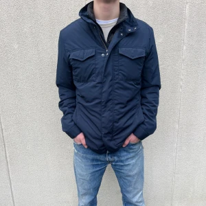 Blå Fieldjacka från Bläck - Snygg blå Fieldjacka från Bläck med hög krage och praktiska fickor framtill. Perfekt för en stilren look under  våren som kommer. Jackan är storlek Medium. Hör av er vid frågor!👍