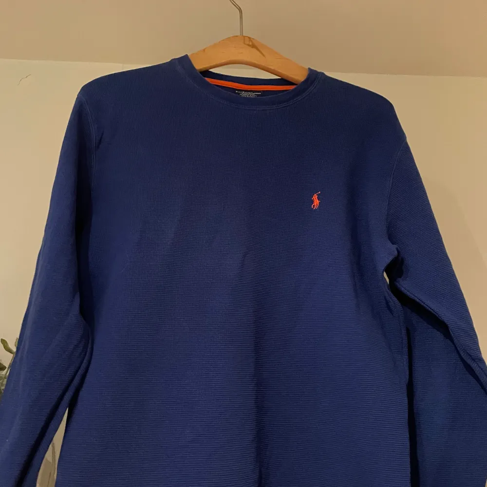 Säljer en snygg blå långärmad tröja från Polo Ralph Lauren. Den är gjord av 100% bomull och har en liten orange broderad logga på bröstet. Perfekt för både höst och vinter. Tröjan är i mycket bra skick och passar perfekt för en avslappnad stil. Använd ett par gånger.. Tröjor & Koftor.