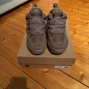 UGG lowmel hickory - Säljer ett par snygga UGG lowmel hickory som är helt nya och aldrig använda. Skorna har en robust design med snörning och är tillverkade i mocka. Perfekta för höst och vår, de ger en stilren look samtidigt som de är bekväma att bära. Passar perfekt för vardagsbruk!