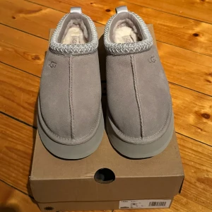 UGG tazz gråa - Säljer grå UGG Tazz som är helt nya och aldrig använda. De har en mysig och varm insida, perfekt för kyliga dagar. Skorna har en stilren design med en robust sula och en dekorativ kant upptill. Perfekta för både vardag och avslappnade tillfällen. Finns i storlekarna 37, 38, 39.
