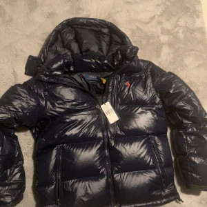 Mörkblå dunjacka från Ralph Lauren - Säljer en snygg och varm svart dunjacka från Ralph Lauren helt  nytt skick. 3500-300 för behöver snabba pengar  så ta chansen nu att få den efterlängtade jackan som alla vill ha för billigt pris. Den är mörkblå men ser svart ut i bilden, Betalning via Swish elr via Plick  och bild på mitt legitimation osv för försäkring att jag är en seriös säljare o detta är inget scam pris kan diskuteras men inte mindre än sån står där uppe för som sagt den är helt ny