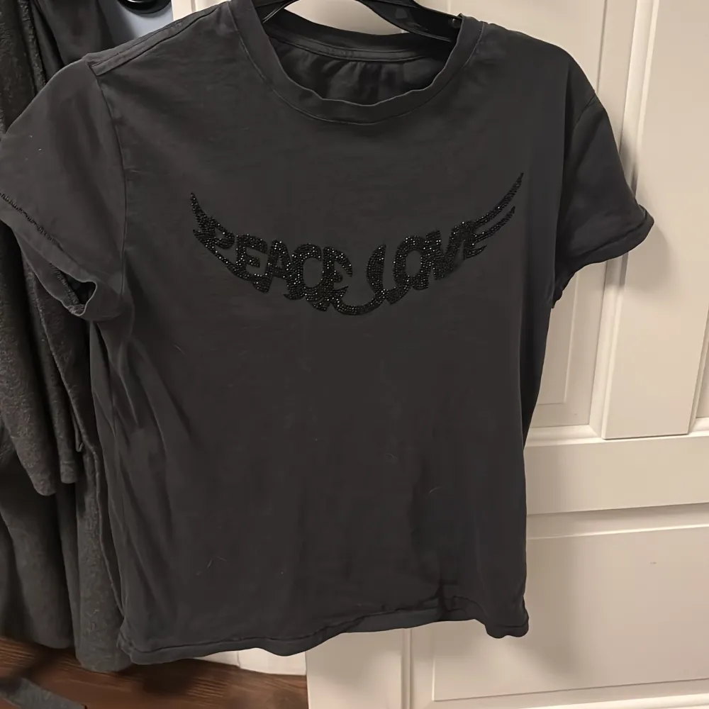 Säljer en svart/grå t-shirt från Zadig & Voltaire med texten 'Peace Love' i glittriga bokstäver på framsidan. T-shirten har en klassisk rund hals och korta ärmar🖤 köparen betalar frakten!. T-shirts.