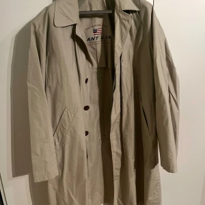 Beige trenchcoat från Gant - Säljer en klassisk beige trenchcoat från Gant i mycket bra skick. Storlek L amerikanskt mått så XL i svensk storlek. Den har en stilren design med knappar framtill och en bekväm passform. Perfekt för höst och vår! 🧥