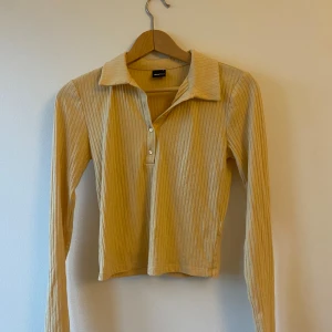 Beige ribbad tröja - Säljer en beige ribbad tröja. Den har en snygg krage och knappar framtill. Tröjan är lite croppad och har långa ärmar, vilket gör den perfekt för höst och vår.