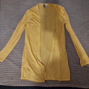 Gul kofta/cardigan från H&M - Säljer en snygg gul kofta från H&M i storlek XS. Den är tunn och perfekt för vår och sommar. Koftan har långa ärmar och en öppen front, vilket gör den enkel att matcha med olika outfits. 