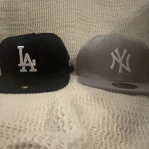 Svart och grå keps från New Era (7” 5/8) - Säljer 2st kepsar (båda för endast 299kr!) eftersom att jag fick dom till bra pris men tyvärr inte min stil. Två kepsar från New Era, en svart med vit LA-logga och en grå med vit NY-logga. Perfekta för både vardag och sportiga tillfällen. Kepsarna har en klassisk passform. OBS helt nya och endast testade