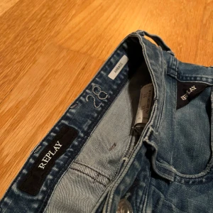 Blå jeans från Replay - Säljer ett par snygga blå jeans från Replay i modellen Anbass. De har en slim passform och är i bra skick med coola slitningar på knäna. Perfekta för både vardag och fest! 