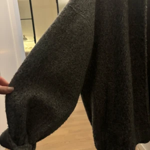 Grå stickad bomberjacka - Mysig grå stickad jacka i bra skick. Perfekt för höst och vinter med sin varma och bekväma design. Jackan har långa ärmar och en lös passform, vilket gör den idealisk för lager-på-lager-stil. Enkel att matcha med olika outfits för en avslappnad look. I Ull 