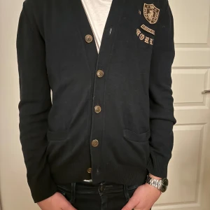 Morris Field Games Cardigan - Säljer en snygg mörkblå cardigan från Morris med broderad logga på bröstet. Den har knappar framtill. Perfekt för både vardag och lite finare tillfällen. 