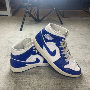 Nike Air Jordans Mid Kentucky Blue - Säljer ett par klassiska Nike Air Jordans i blått och vitt. Skorna har en snygg design med snörning och den ikoniska loggan på sidan. Perfekta för både vardag och sportiga tillfällen. Sulan är i bra skick och ger bra grepp. Passar dig som vill ha stil och komfort i ett! Nypris är 2600+, ställ gärna frågor!