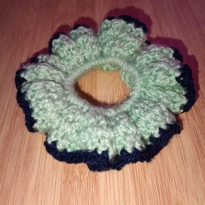 Virkad scrunchie - Snygg och unik virkad scrunchie i grönt. med mörkblå detaljer. Perfekt för att ge din frisyr en färgglad touch. Den är elastisk och passar de flesta hårtyper. Perfekt accessoarer för både vardag och fest! Skulle du vilja ha en i en specifik färg är det bara att skriva. Alla accessoarer är gjorda av mig.
