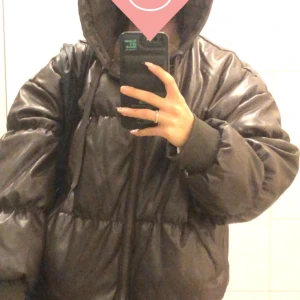 Brun pufferjacka - Säljer en svart pufferjacka från H&M i storlek S. Jackan är perfekt för kalla dagar med sin tjocka vaddering och har en praktisk dragkedja framtill. Den har en stor huva och långa ärmar för extra värme. Perfekt för vintern! 🖤