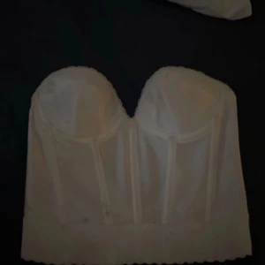 Vit korsett - Snygg vit korsett i ett stilrent och klassiskt snitt. Den är axelbandslös och har en strukturerad design med synliga sömmar som ger en elegant look. Perfekt för att bära under en klänning eller som en statement piece till fest.