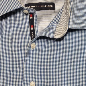 Blårutig skjorta från Tommy Hilfiger - Säljer en snygg blårutig skjorta från Tommy Hilfiger i mycket bra skick. Skjortan har långa ärmar och klassiska knappar framtill. Perfekt för både vardag och fest! Den är gjord i ett skönt bomullsmaterial som andas bra. Passar perfekt till jeans eller chinos för en stilren look.