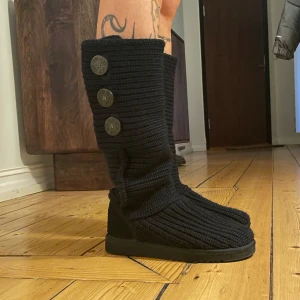Svarta stickade boots från UGG Cardy knit - Säljer ett par svarta stickade boots från UGG i mycket bra skick. De har tre stora knappar på sidan och en bekväm, mjuk sula i ull. Perfekta för höst och vinter. Synts på lovisa worge bla