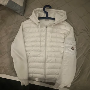 Vit moncler cardigan - Säljer en snygg vit jacka från moncler. Helt fel fri förutom ett litet hål i högra fickan men inte rakt igenom så inget kan trilla ut. Den säljs relativt billigt jämfört med andra moncler jackor då ja saknar kvitto men allt stämmer som det ska med jackan. Strl 2 som motsvarar S i herr
