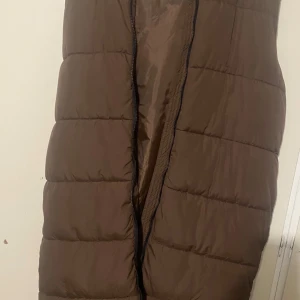 Brun dunväst från Brave Soul - Säljer en brun dunväst från Brave Soul i storlek XL. Västen är perfekt för kyliga dagar och har en praktisk dragkedja framtill. Den är i mycket bra skick och passar perfekt för höst och vinter. En stilren och varm väst för alla tillfällen!