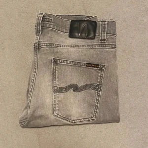 Grå jeans från Nudie Jeans - Säljer ett par grå jeans från Nudie Jeans i bra skick. De har en snygg faded look och klassisk femficksdesign. Perfekta för både vardag och fest! Passformen är slim och de är tillverkade i bomull för en bekväm känsla. Modellen: Lean Dean|| strl 30/32|| Pris kan ändras vid snabb affär 🤝