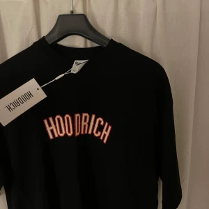 Svart t-shirt från Hoodrich - Säljer en svart t-shirt från Hoodrich i storlek S men oversize . Den har en cool text 'HOODRICH' tryckt på framsidan och baksidan, samt texten 'FROM NOTHING TO SOMETHING' längs ryggen. Perfekt för en avslappnad stil!