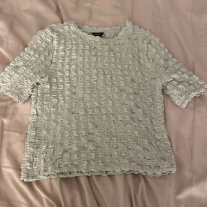 Beige topp från Lindex - Säljer en superfin beige topp från Lindex i storlek S. Den har ett unikt rynkat mönster och korta ärmar, perfekt för både vardag och fest. Toppen är i mycket bra skick och passar perfekt till både jeans och kjol. Skicka ett meddelande vid intresse! ✨